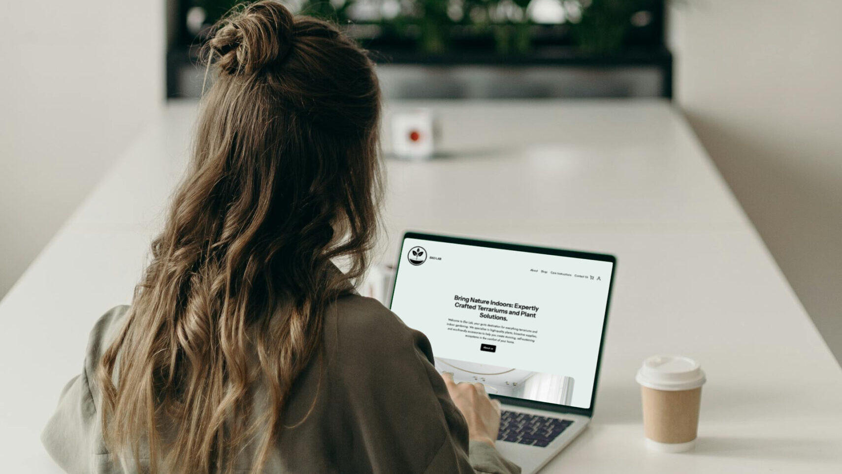 Woman sitting at computer browsing website, plants in background