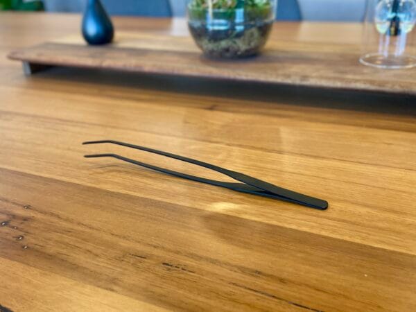 Eko Lab premium black stainless steel tweezers, on a wooden table