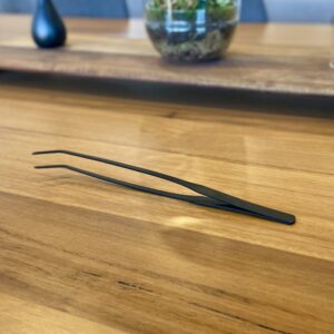 Eko Lab premium black stainless steel tweezers, on a wooden table